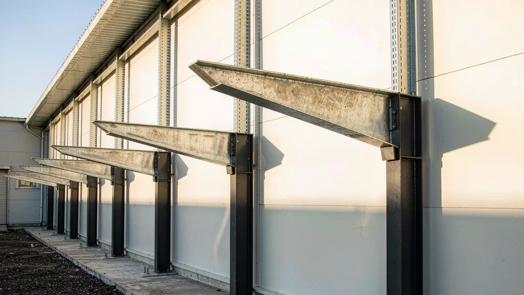 Close-up of a cantilever steel canopy with tapered beams, bolted base plates and galvanized purlins
