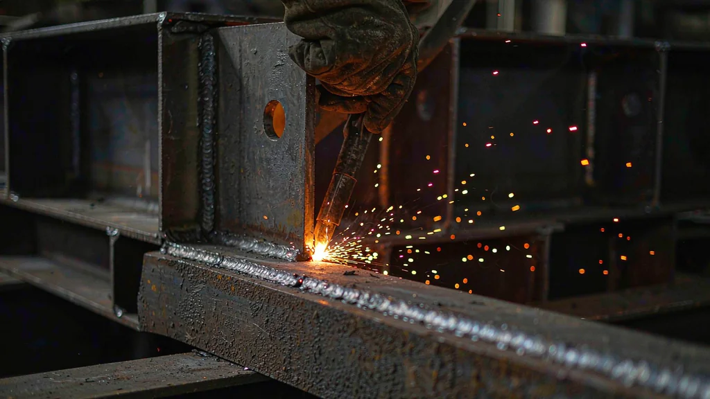 Welder depositing a full-penetration weld on a fabricated structural steel column connection in a factory